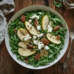 Overhead bowl of arugula pear salad with pear slices and pecans