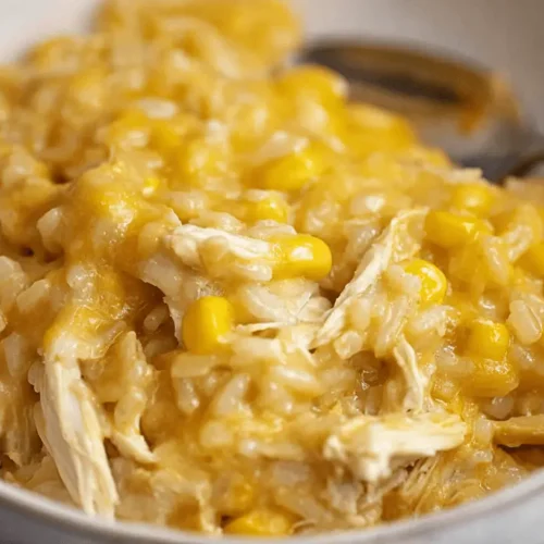 Easy Cheesy Chicken and Rice Crockpot Recipe 2 A close-up, top-down view of a hearty bowl of cheesy chicken and rice crockpot, featuring shredded chicken, corn, and a rich, yellow-orange cheesy sauce.
