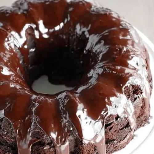Moist Chocolate Bundt Cake Recipe 2 A decadent, freshly glazed chocolate bundt cake on a white cake stand.