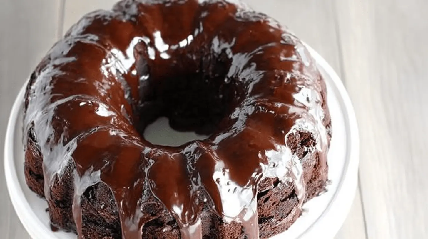 Moist Chocolate Bundt Cake Recipe 1 A decadent, freshly glazed chocolate bundt cake on a white cake stand.