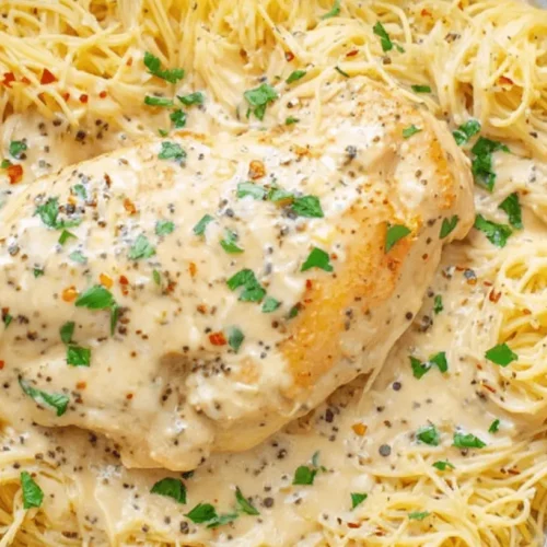 Easy, Creamy Crock Pot Angel Chicken Recipe 2 Close-up of a delicious Crock Pot Angel Chicken dish on a round plate, featuring creamy chicken, thin pasta, and fresh parsley garnish.