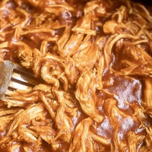 The Best Easy Crockpot BBQ Chicken Recipe 2 Close-up of shredded crockpot BBQ chicken being stirred with a fork, coated in rich, glossy sauce.