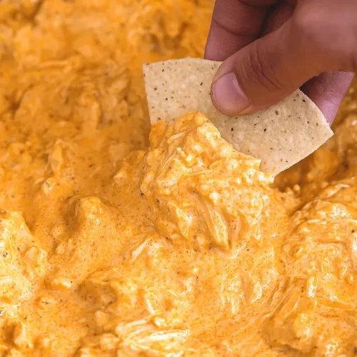 Ultimate Crockpot Buffalo Chicken Dip Recipe 2 Hand scooping creamy crockpot buffalo chicken dip with a tortilla chip.
