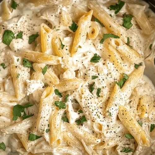 Easy Crockpot Chicken Alfredo Recipe 2 Appetizing close-up of creamy crockpot chicken alfredo with penne pasta, chicken, pepper, and herbs in a dark pot.