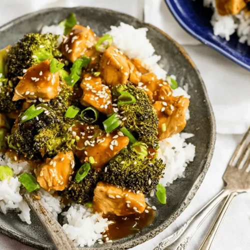 Overhead shot of delicious Crockpot Chicken and Broccoli served over white rice on a rustic plate, garnished with sesame seeds and scallions.