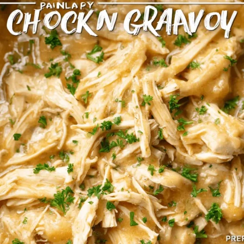 Close-up of a creamy shredded crockpot chicken and gravy dish, garnished with fresh parsley in a dark slow cooker.