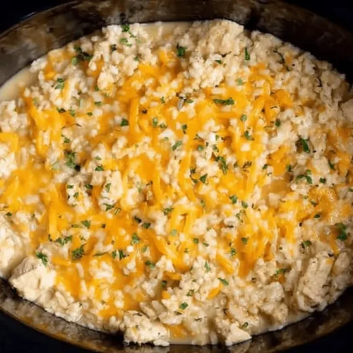 A creamy crockpot chicken and rice casserole with melted cheese and fresh parsley, served in a black slow cooker insert.