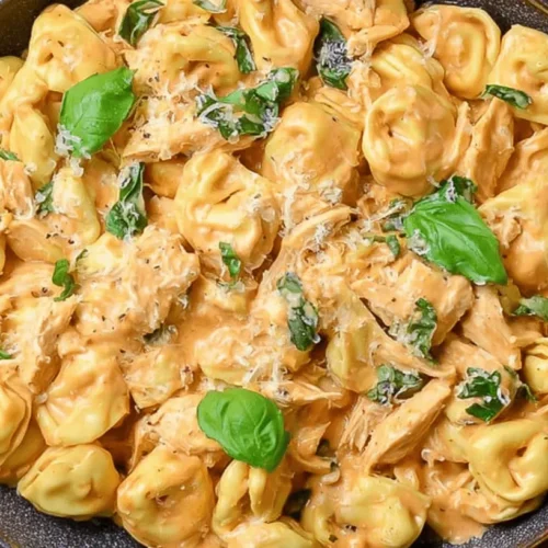 Creamy CrockPot Chicken Tortellini with fresh basil and grated cheese in a rustic bowl.