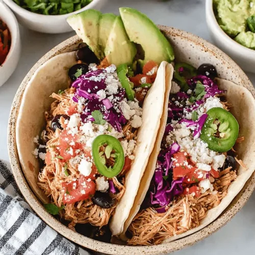 Easy Crockpot Shredded Chicken Tacos: Flavorful & Fast 2 Overhead view of two vibrant crockpot shredded chicken tacos in a rustic bowl, garnished with fresh toppings like cheese, pico de gallo, and cilantro, served with guacamole and lime.