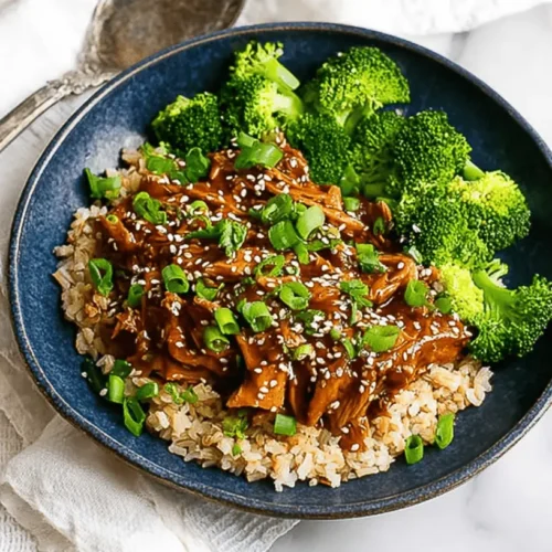Appetizing bowl of slow cooker honey garlic chicken, served with brown rice and broccoli, garnished with green onions and sesame seeds.