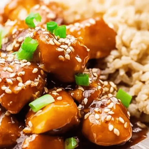 Appetizing slow cooker orange chicken garnished with sesame seeds and green onions, served alongside brown rice.