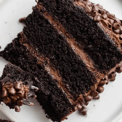 Ultimate Triple Chocolate Cake Recipe 2 Decadent slice of triple chocolate cake with rich frosting and chocolate chips, being enjoyed with a fork.