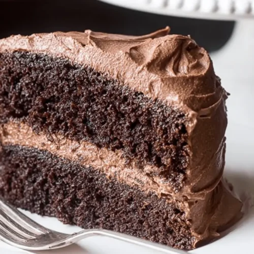 Best Moist Vegan Chocolate Cake Recipe – Ready in 30 Minutes 2 A decadent slice of vegan chocolate cake with rich, creamy frosting on a white plate.