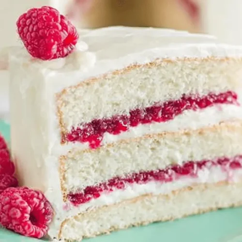 White Chocolate Raspberry Cake 2 A beautifully presented slice of white chocolate raspberry cake with creamy frosting and fresh raspberries on a mint green plate.