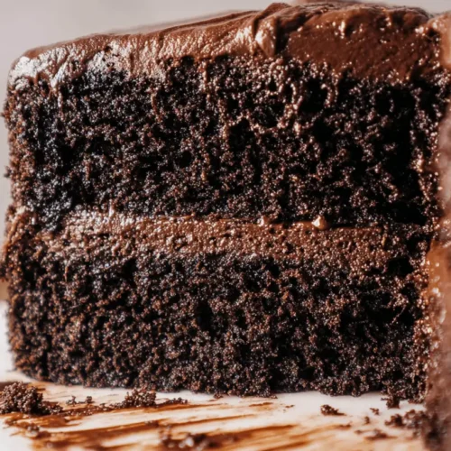 The Yummiest Chocolate Cake: A Decadent Portillo's Copycat Recipe 2 A close-up of a slice removed from a rich, multi-layered yummiest chocolate cake with decadent frosting and crumbs on a white plate.