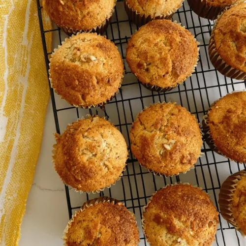 Overhead shot of golden-brown banana nut bread muffins cooling on a black wire rack, perfect for a homemade banana nut bread recipe.