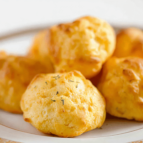 simple Cheese Puffs Recipe taken with an old camera, golden-baked puffs, savory crisp texture, herb speckles, elegant white plate, ornate gold rim, sharp focus, shallow depth of field, bright lighting, clean white background.