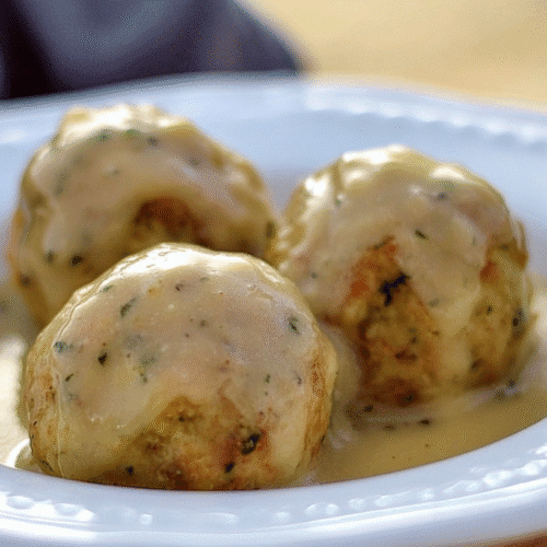Turkey Stuffing Balls: Easy Recipe for Leftovers or Fresh 4 simple Turkey stuffing Balls taken with an old camera, appetizing close-up, creamy glossy sauce, white embossed ceramic bowl, soft diffused warm lighting, shallow depth of field, wooden surface, comforting.