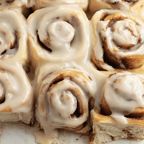 Delicious Banana Bread Cinnamon Rolls Recipe 4 simple banana bread cinnamon rolls taken with an old camera, freshly baked, creamy spiced icing, golden-brown, soft layered interior, classic spiral, tender dough, glistening cinnamon sugar, pillowy, crisp edges, luscious off-white frosting, pooling, delicate drips, bright even lighting, warm tones, white background.