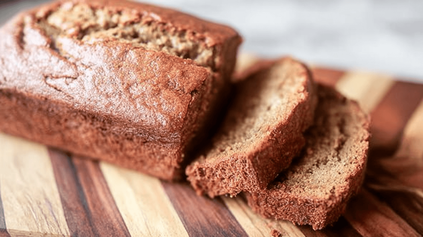 Stacked banana bread French toast topped with sliced bananas, whipped cream, and maple syrup.