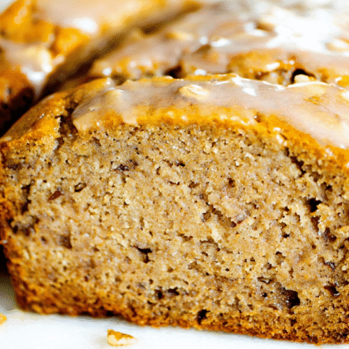 simple low sugar banana bread taken with an old camera, close-up, high-angle, partially sliced, generous translucent glaze, warm golden-brown crust, moist medium-brown crumb, chopped nuts, bright soft lighting, out-of-focus white background, homemade comfort.