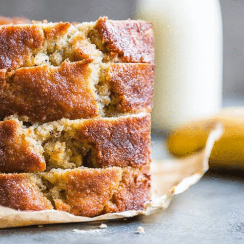 simple paleo banana bread taken with an old camera, close-up, stacked golden-brown slices, caramelized rustic crust, moist golden-yellow crumb, visible mashed banana, crumpled parchment, dark stone surface, blurred ripe bananas, blurred milk jug, soft grey-blue background, shallow depth of field, inviting warm light.