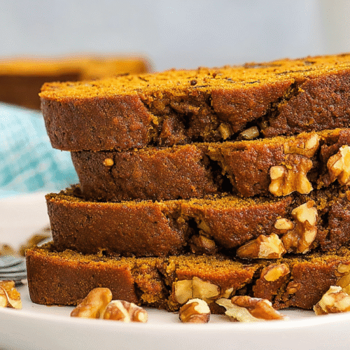 simple pumpkin banana bread taken with an old camera, five thick slices, stacked, round white plate, warm golden-brown hue, caramelized edges, moist crumb, visible walnuts, scattered walnuts, silver fork detail, blurred original loaf, light blue and white checkered fabric, soft diffused natural light, cozy atmosphere.
