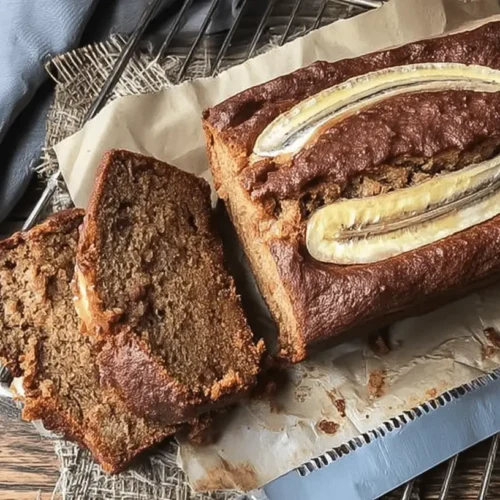 The Ultimate Moist Banana Bread Recipe 2 Freshly baked moist banana bread recipe loaf and slices on a rustic wooden board with banana garnish.