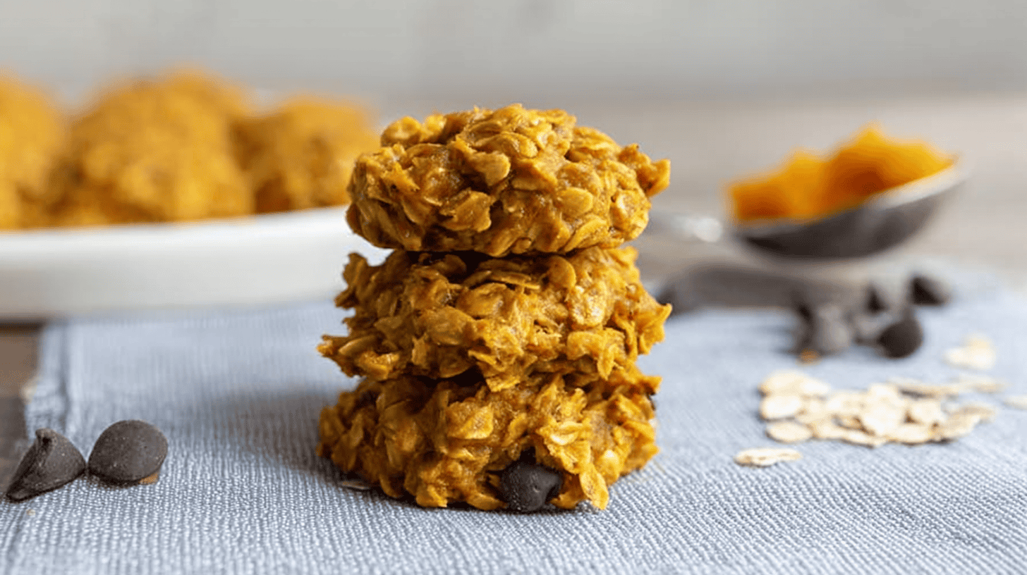 Delicious No Bake Pumpkin Cookies: Easy & Quick Recipe 1 simple No Bake Pumpkin Cookies taken with an old camera, stack of three chunky golden-brown cookies, distinct rolled oats texture, rustic wholesome, warm orange-yellow undertones, pale blue-grey woven fabric, scattered chocolate chips, metallic spoon with vibrant pumpkin puree, soft natural light, shallow depth of field, cozy autumnal baking scene.