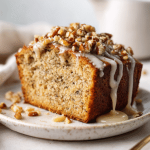 The Best Keto Banana Bread Recipe (Low-Carb & Delicious!) 4 Slice of keto banana bread on a white plate with walnut topping and vanilla glaze.